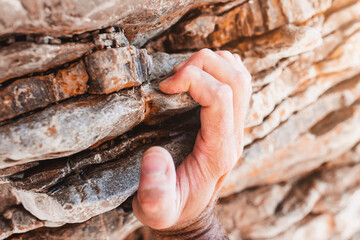Strong male fingers cling to a rock ledge - close-up rock climbing