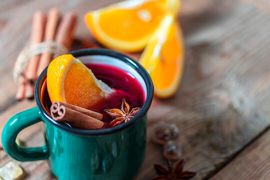 Hot Christmas mulled wine with orange slices, cinnamon, anise and spices in a green rustic mug on a wooden background.