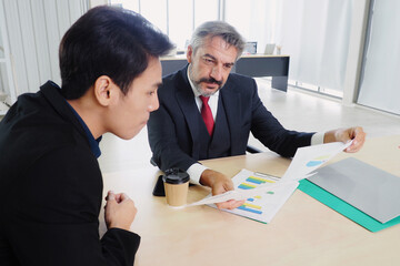 Senior male manager and his Asian colleague meeting and analyzing data and sales record documents of the company in the office Business planning and working lifestyle concept