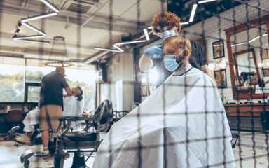 Man getting hair cut at the barbershop wearing mask during coronavirus pandemic. Professional barber wearing gloves. Covid-19, beauty, selfcare, style, healthcare and medicine concept.