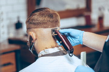 Man getting hair cut at the barbershop wearing mask during coronavirus pandemic. Professional...