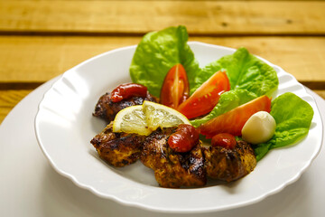 White plate with slices of grilled meat with lemon and tomato decorated.