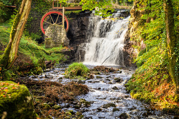Vintage red waterwheel with waterfall in autumn colours in Glenariff Forest Park, Count Antrim, Northern Ireland - obrazy, fototapety, plakaty