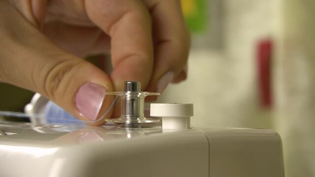 A female hand puts a bobbin on the winder of the sewing machine to automatically wind blue thread. Winding the sewing machine bobbin. Close-up. Camera movement from right to left .
