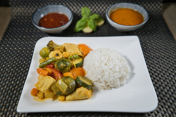 Eine Portion gelbes Reis Curry mit Hühnchen und frischem biop gemüse auf einem weißen Teller,...