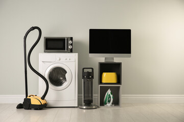 Modern vacuum cleaner and different household appliances near light wall indoors