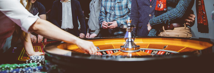 People play poker roulette at the table. Friends playing in the casino. A group of young people at a roulette table with a tape measure. Table for gambling in a luxury casino. Gambling.Casino roulette