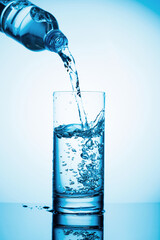 Pouring water from a bottle into glass on a blue background.