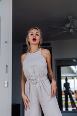 Outdoor portrait of rich caucasian woman in classic jumpsuit with red lipstick on vacation outside villa hotel.  