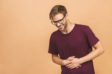 Young man in pain holding his hurting stomach isolated on the beige background. Abdominal pain.