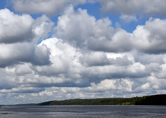 Obraz premium Blue sky with beautiful white clouds over a wide river. Ripples on the surface of the water. Low cloud. Green forest on the banks.