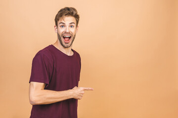 Look over there! Happy young handsome bearded man in casual pointing away and smiling while standing against beige background.