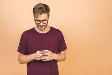 Always in touch. Happy young man in glasses typing sms on beige background, smiling.