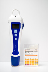A modern digital pH meter next to a box of paper pH strips. pH measuring.

Translation right box: 