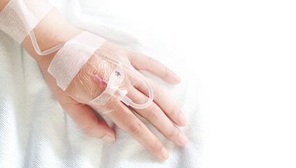Close-up of saline solution in a patient's hand in clothing, lying on a hospital bed, the patient dripping saline on a white background.