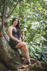 Hermosa mujer joven morena con un vestido de color negro sonriendo en un entorno con mucha  naturaleza