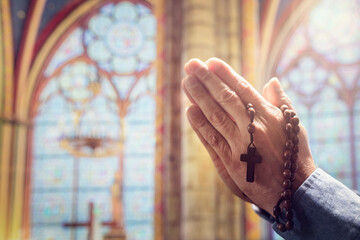 Hands folded in prayer in church with rosary beads and religious cross