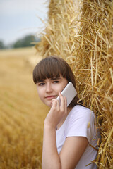 A young girl is talking on the phone with her back against the straw.