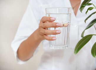 Close up photo of woman's hand with glass of water in a white robe.