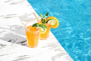 Refreshing cocktail in glasses near outdoor swimming pool on sunny day