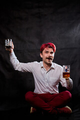Young handsome guy with red hair in white shirt drinking beer. Funny man with emotions on the face and two beer mugs in hands and black background