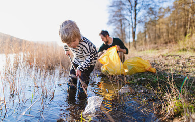 Father with small son collecting rubbish outdoors in nature, plogging concept.