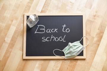 Blackboard with handwritten label "back to school", facial mask and bottle of hydroalcoholic gel. Protective elements for returning to classrooms.