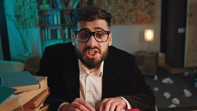 Concentrated man with eyeglasses in the library looking straight to the camera speaking with expression then he continue to type something on his typewriter