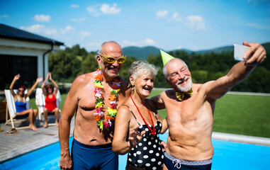 Obraz na płótnie Canvas Group of cheerful seniors by swimming pool outdoors in backyard, taking selfie.