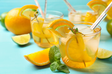 Delicious refreshing drink with orange and lime slices on light blue table, closeup