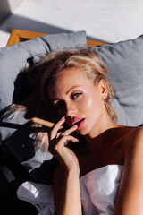 Fashion outdoor portrait of naked woman sit on sofa cover herself with blanket holding cigar,...