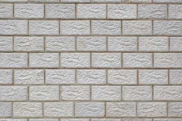 The wall of the house is made of gray concrete blocks. Background or wallpaper. The seams form a pattern similar to brickwork. Light backdrop on the topic of housing construction and renovation