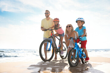 Fototapeta premium Happy parents teaching children to ride bicycles on sandy beach near sea