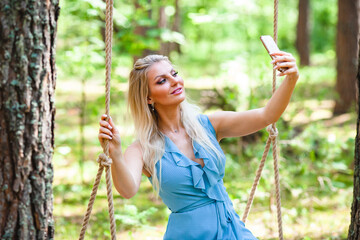 Beautiful blond woman in blue dress using smartphone to taking selfie