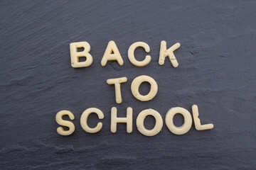 Back to school. Letters cut out of cheese on black background.