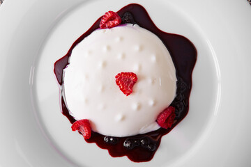 panna cotta on white plate with berry sauce
