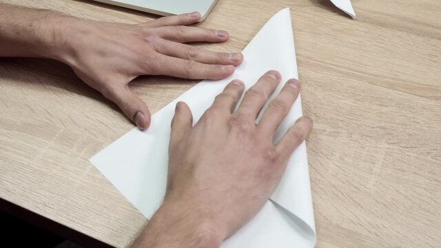 Close-up of man folding origami paper. Stock footage. Men's hands are folded from white paper origami or airplane. Origami class during break at work