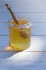 A jar of fresh honey with a wooden honey spoon on a white wooden background. Sweet sticky healthy product. Vertical orientation.