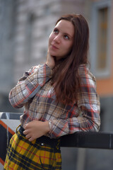 slender brunette girl in a plaid skirt and blouse in the summer on the bridge