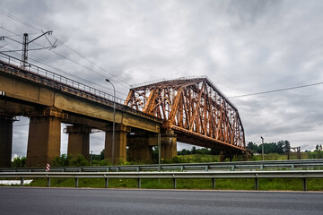 Landscape with iron railroad bridge in Dmitrov district. Highway under the bridge. Massive railway structure
