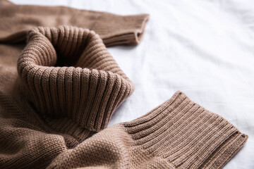 Brown warm sweater on white crumpled fabric, closeup