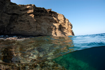 Fototapeta na wymiar Split shot of a rocky island with clear waters and a blue sky.