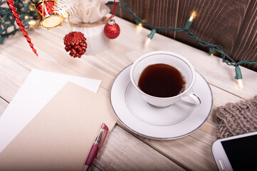 Cup of coffee, cellphone, 
blank paper, pen and Christmas tree on wooden table.
 holiday home decor concept.