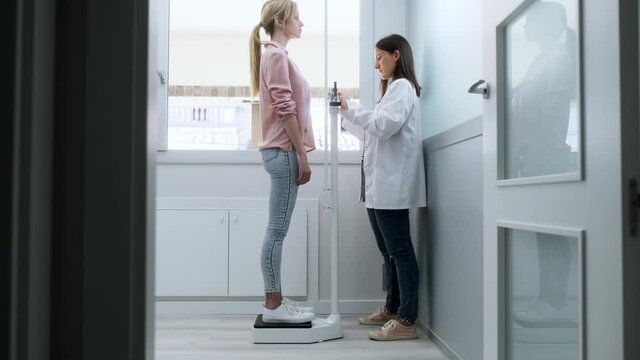 Video of beautiful young nutritionist woman weighing and measuring his patient on the scale in consultation.