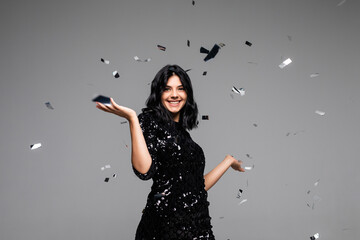 Cheerful young woman is stretching out her hands while confetti falling on her isolated on gray background