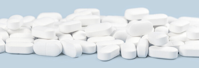 many white capsule tablets or pills on blue table. Close up. Healthcare pharmacy and medicine concept with copy space Painkillers or prescription drugs consumption. Medical Web banner