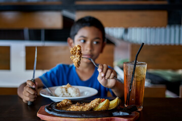 Fototapeta na wymiar Cute boy eating grilled Chicken steak on stoned plate in restaurant
