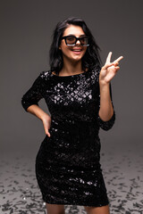 Beautiful young woman with posing in sunglasses, black mini dress isolated on gray background