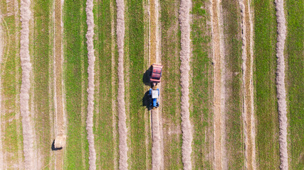 Aerial view of tractor with baler rolling bales of straw on harvested field. Top view.