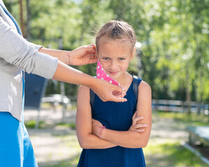 Fototapeta premium Thoughtful woman wears a protective mask on a disgruntled daughter. Girl goes back to school